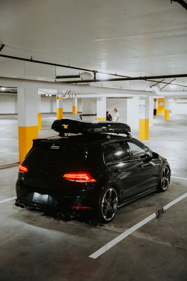 Stylish black car with a roof rack parked in a dimly lit underground garage.